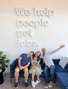 group of three people sitting on couch under sign that says we help people get jobs