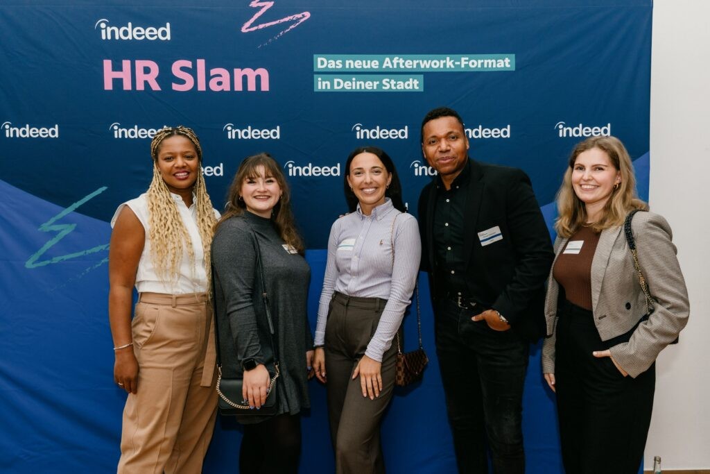 Serah with other smiling attendees posing together in front of an Indeed "HR Slam" event backdrop, described as an after-work format coming to cities across Germany.