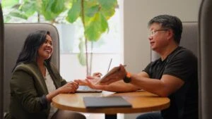 A businesswoman and businessman collaborate using both a laptop and a digital tablet in a modern, green office setting.