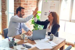 Two colleagues high fiving each other while sitting at a table