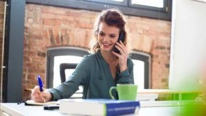 Woman in office setting talking on the phone and writing down notes