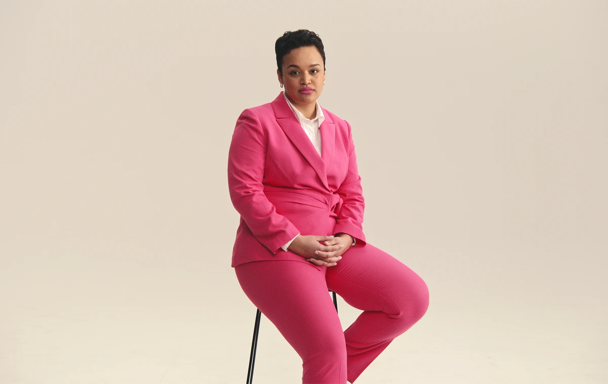 African american woman sitting on a stool wearing a pink pantsuit