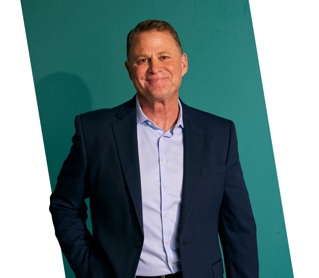 A man wearing a suit smiles with one hand in his pocket and the other hand by his side