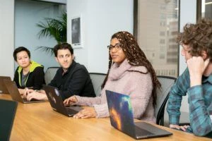 Four employees with laptops meeting at a conference table