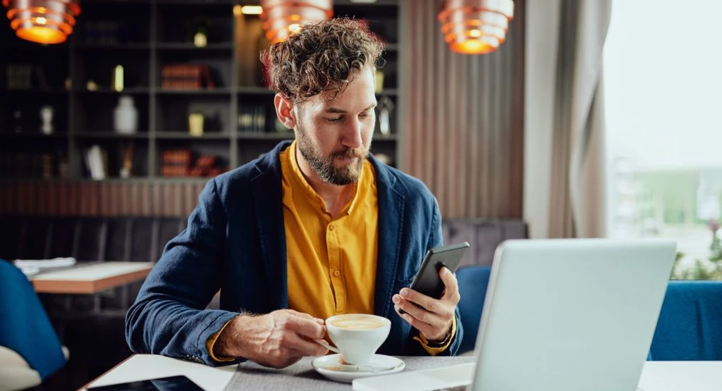 Man working in a coffee shop looking at his phone.