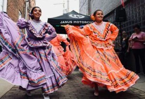 Two Hispanic women dancing in authentic dresses at event.
