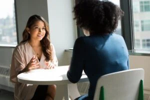 Two people sitting across from each other at a round table and having a conversation.