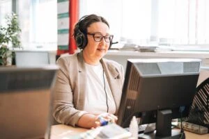 Smiling middle aged brunette woman in headset with headphones and microphone working at computer in the office