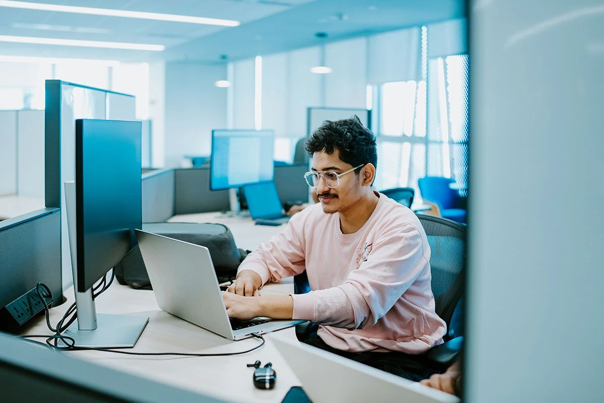 Person working on a laptop and desktop computer in a modern office environment