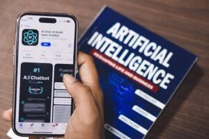 An artificial intelligence book on a desk, with a phone opened to the App Store with an AI chatbot app.