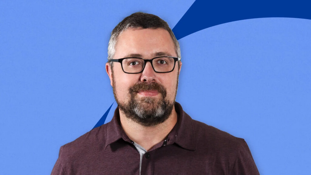 Indeed’s Head of Responsible AI Trey Causey. He’s a smiling white man in glasses with short brown and white hair and a beard, wearing a maroon collared shirt.
