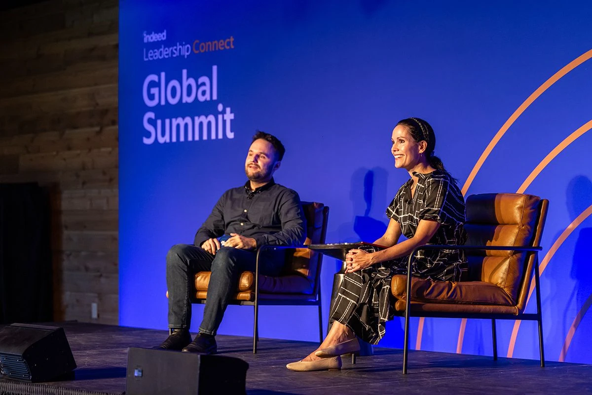 Two speakers are seated on stage at the Indeed Leadership Connect Global Summit, engaging with the audience
