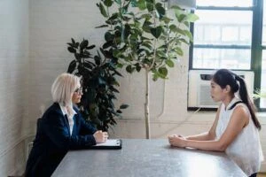 Two women sitting around a desk speaking with each other
