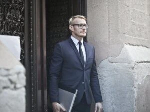 Man in suit holding a laptop standing outside a building