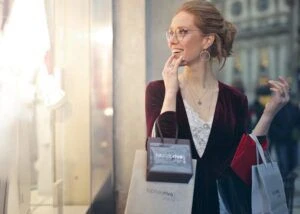 A smiling woman holding shopping bags and looking through a storefront window