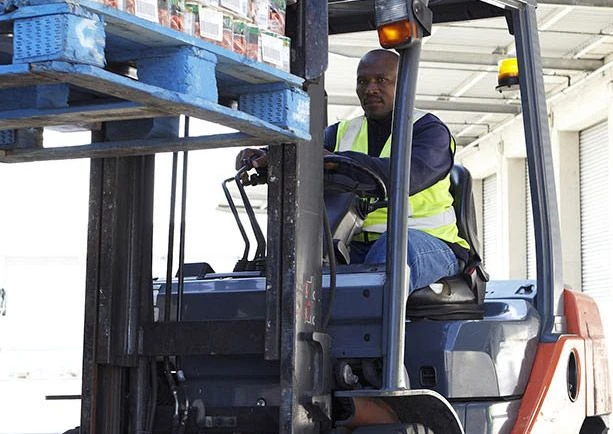 A Black, male worker uses a forklift