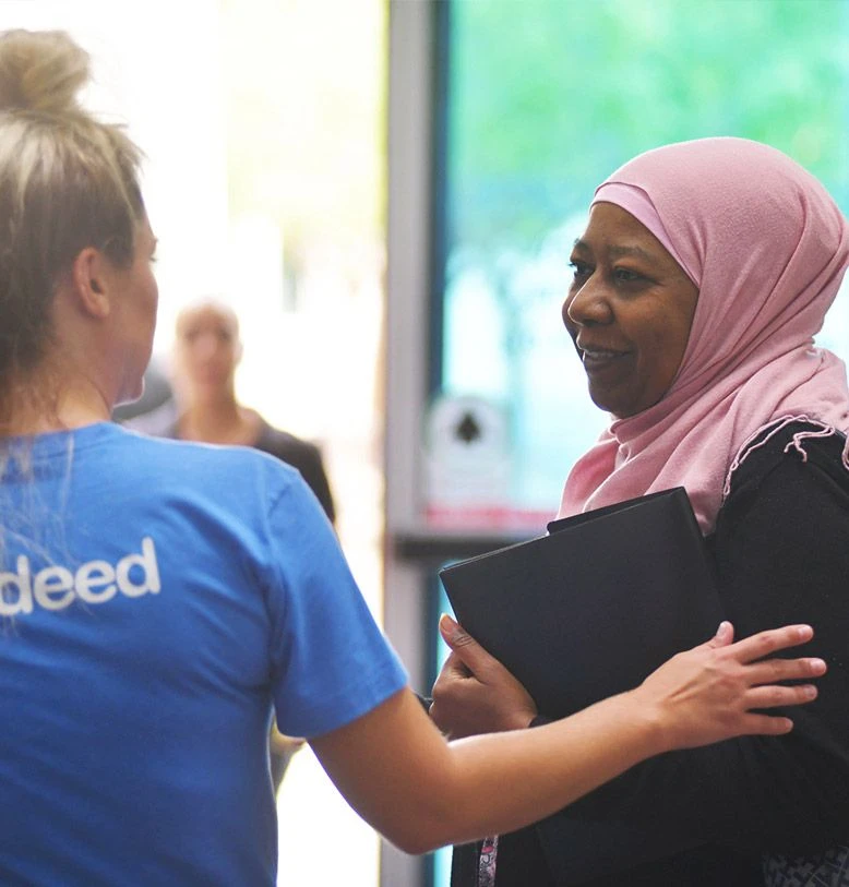 A woman wearing a hijab and a person wearing an Indeed shirt have a discussion