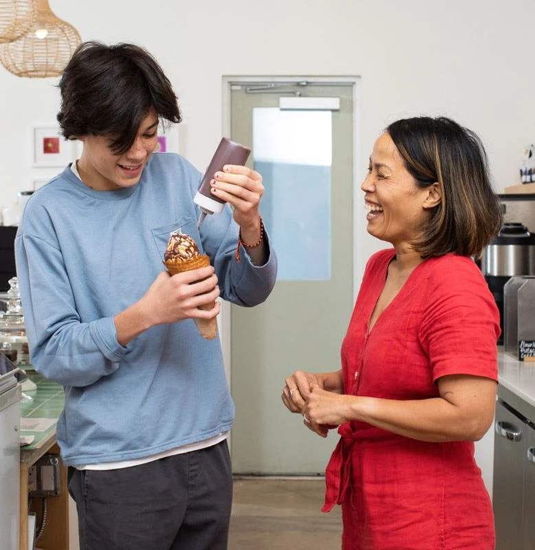 An older, Asian woman trains a younger employee on how to prepare an ice cream cone