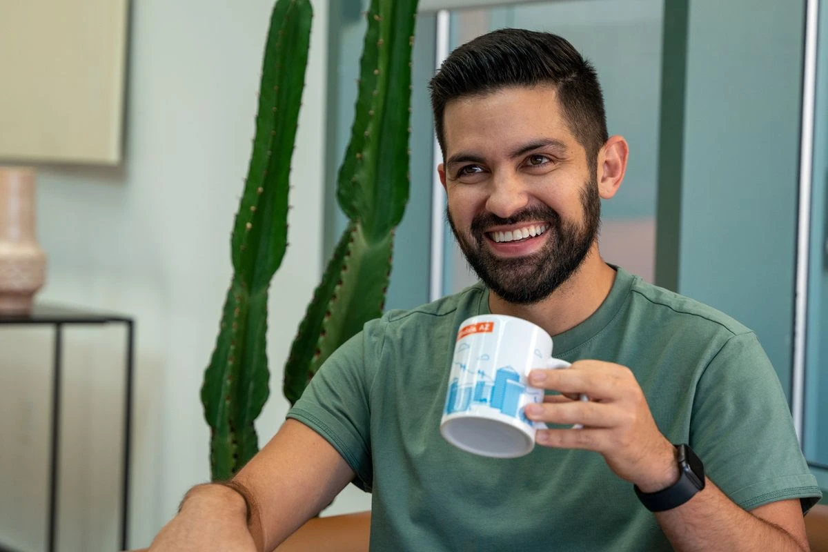 Person smiling and holding an Indeed mug, seated indoors with a cactus in the background.