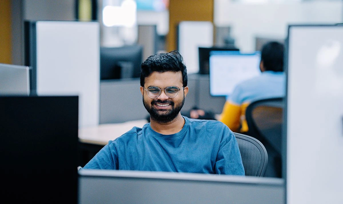 A person wearing glasses and a blue t-shirt sits at a desk in an office setting