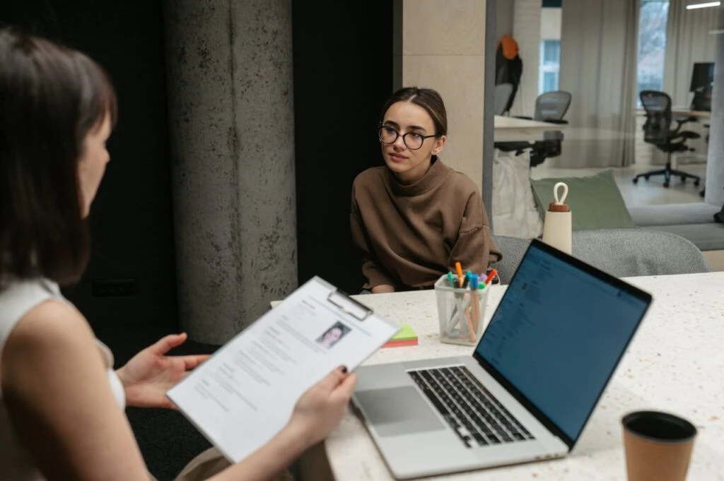 woman speaning with a person at desk. Looking at resume. Interview