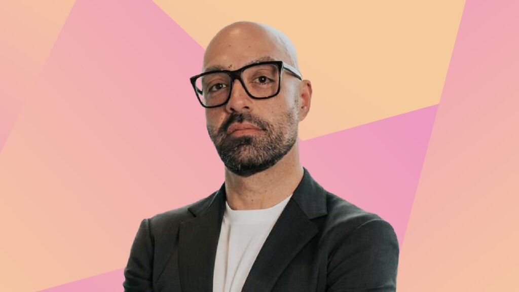 Areyh Lehrer is a man with a shaved head, dark short beard, and black-framed glasses. He is wearing a grey blazer.