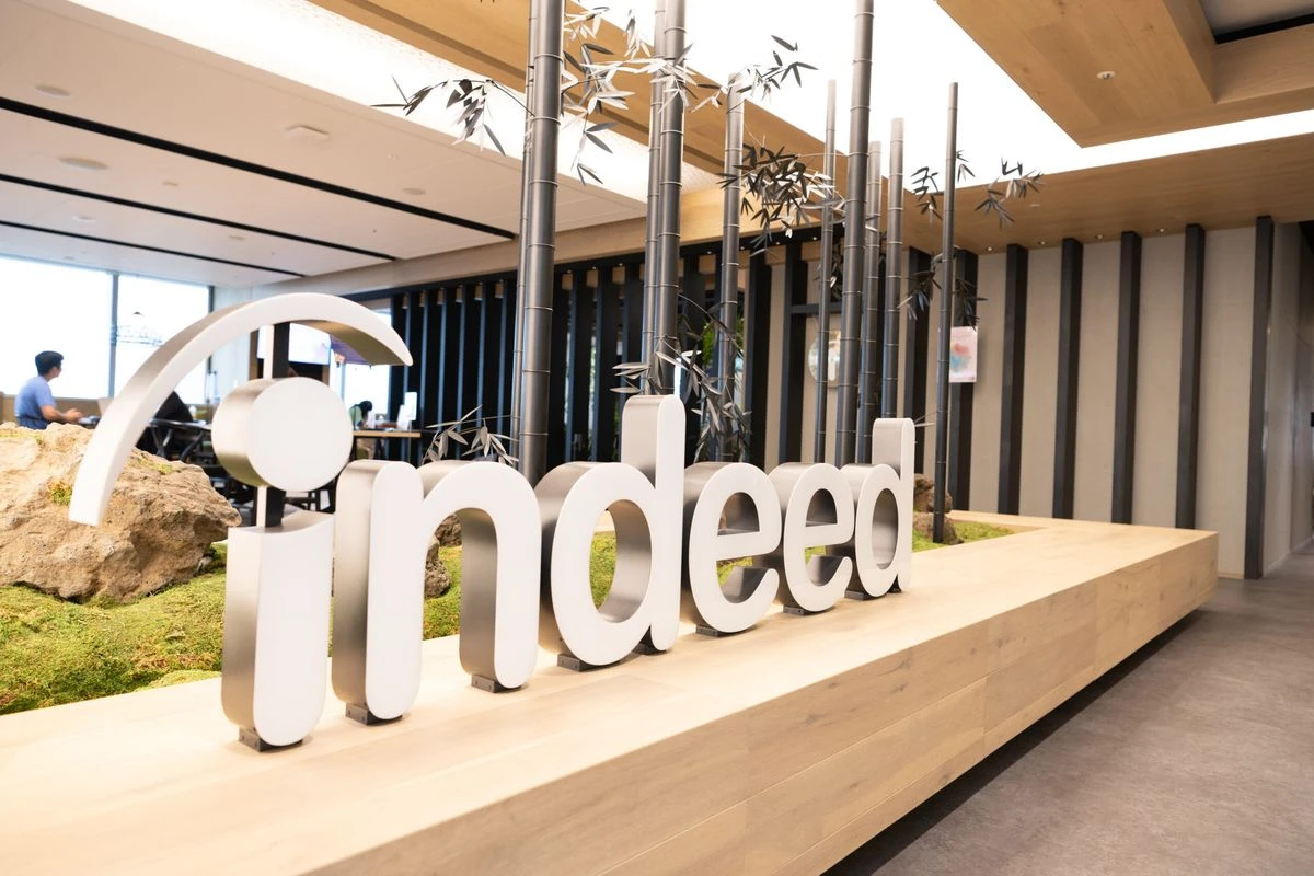A large, 3D Indeed logo sign positioned in a modern office interior featuring an indoor moss garden with decorative black bamboo-like poles.