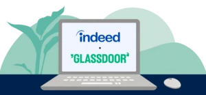A laptop open on a desk, featuring the Indeed and Glassdoor logos on its screen