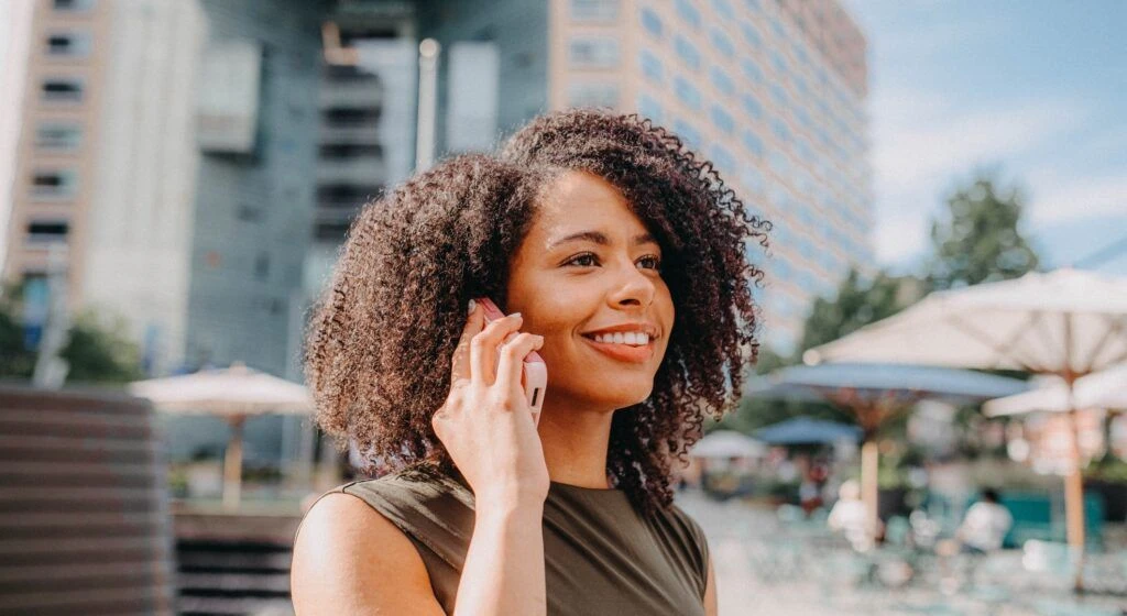 woman smiling while holding a cell phone to her ear, in a city environment