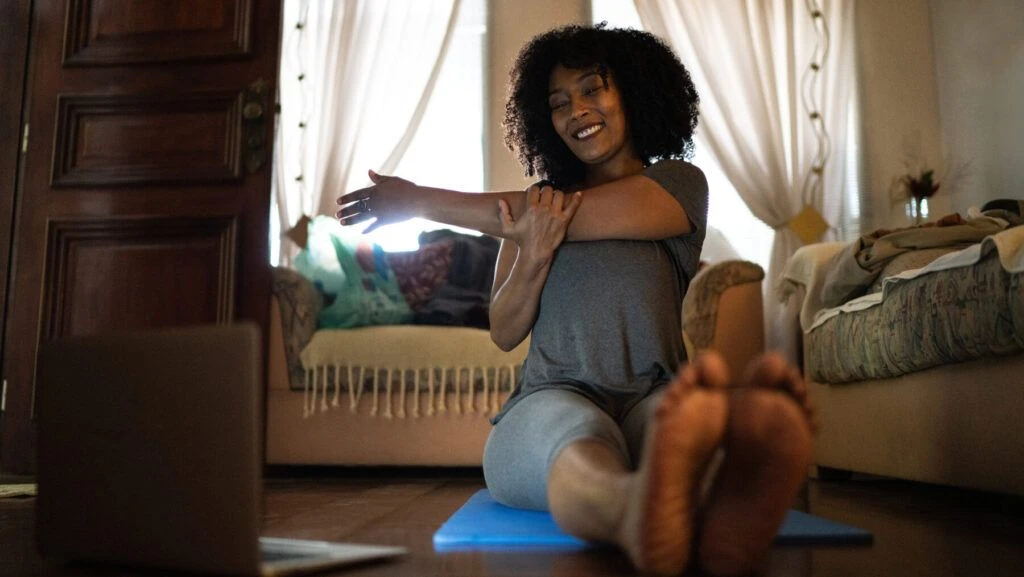 Woman sitting on the floor doing yoga at home while watching a virtual yoga class on her laptop