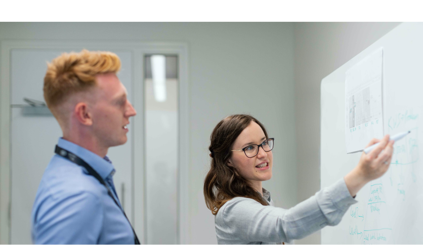 woman writing on a whiteboard and man watching