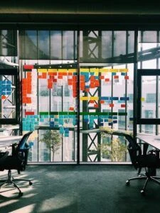 A glass window being used as an agile task board filled with color-coded sticky notes in different columns
