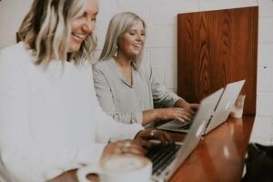 Two women smiling and collaborating on their laptops