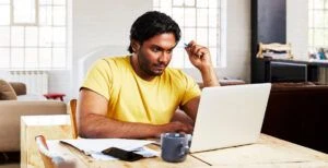 Male job seeker is wearing a yellow shirt and working on his computer.