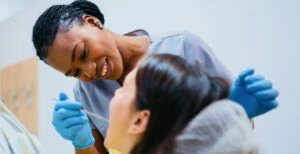 Dentist wearing blue scrubs and gloves looking into patient's mouth.