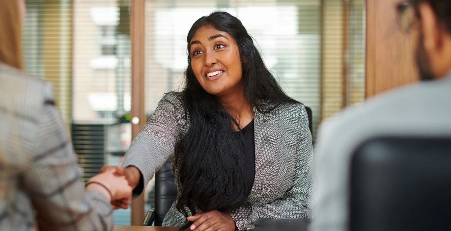 Female job seeker smiling and shaking hands with interviewer.