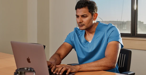 Male healthcare worker in blue scrubs looking at computer