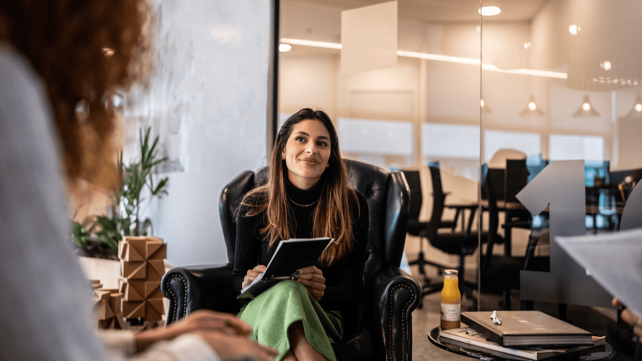 A woman sitting down, listening to her colleagues in an office workspace.