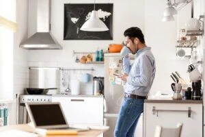 Man drinking coffee at home in kitchen while working