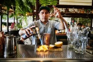 bartender using hand torch to create craft cocktails at bar in restaurant