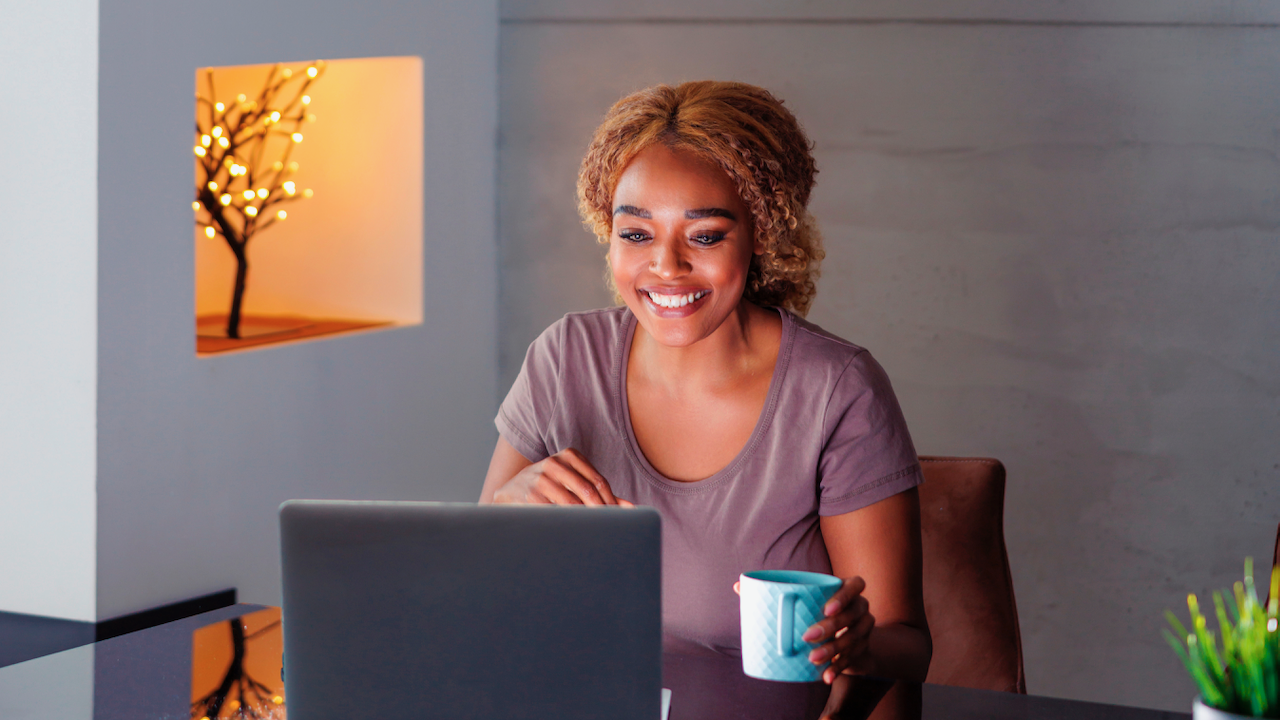 Une femme qui regarde son écran avec une tasse bleu-vert dans un lieu de travail