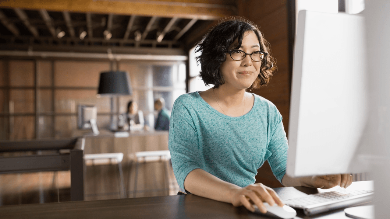 Une personne en haut vert et lunettes assise devant un ordinateur de bureau