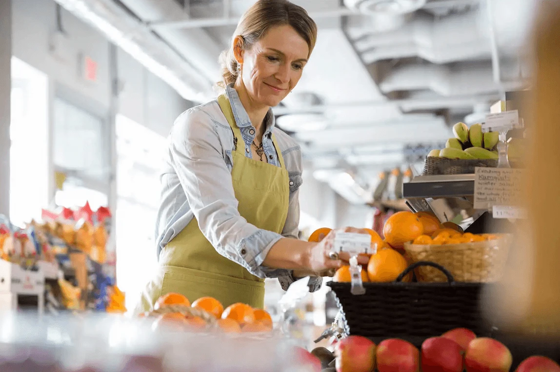 Blonde woman in yellow apron arranging fruit stall