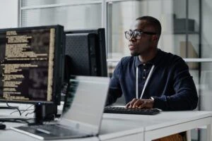 Computerbildschirm mit Code und Person im Hintergrund am Schreibtisch