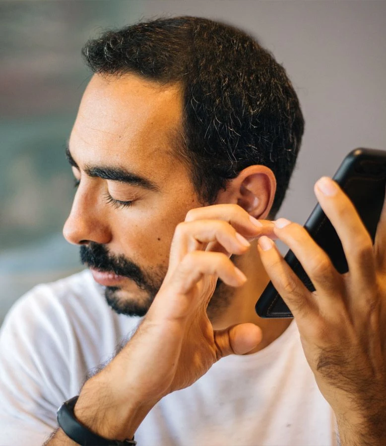 En mørkhåret mand med skæg lytter med lukkede øjne opmærksomt til sin telefon og det hjælpeprogram, han bruger