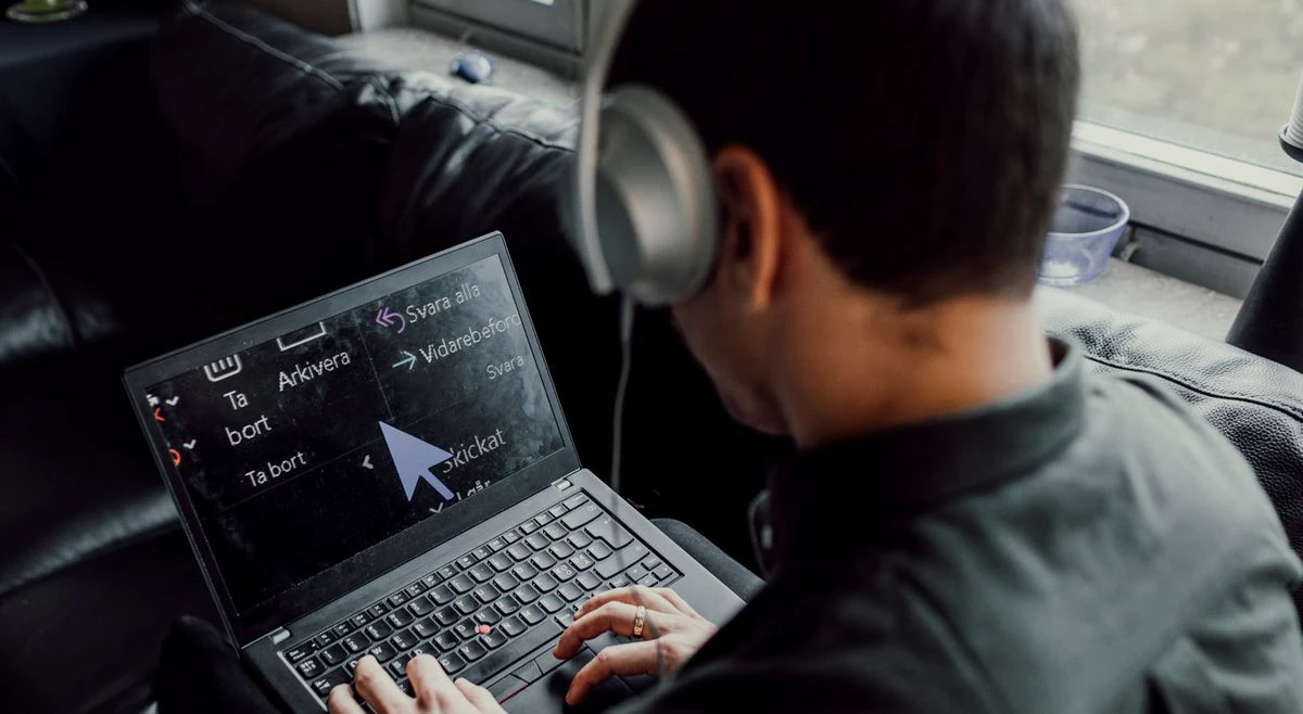 En person med kort, sort hår sidder afslappet og bruger sin forstørrelsesteknologi og sine hovedtelefoner i en browser på sin bærbare computer