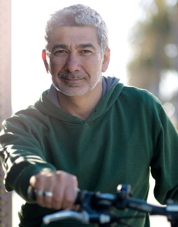 Un homme d'âge mûr à vélo, vêtu de manière décontractée, regarde l'objectif