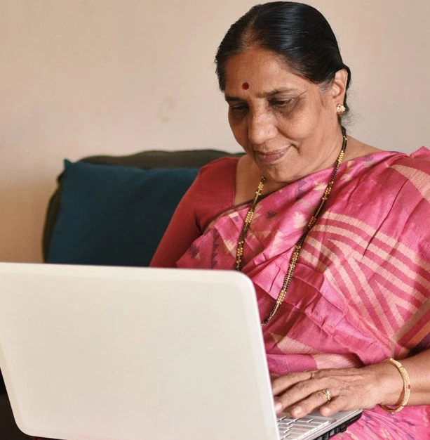 Une femme d'Asie du Sud vêtue d'un sari utilise son ordinateur portable, assise sur un canapé