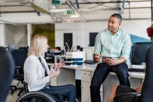 A photo of a businesswoman with a disability sharing ideas with coworker. Male professional is holding digital tablet. They are in creative office.