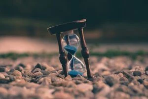 An hourglass with blue sand sitting on a bed of rocks at a beach